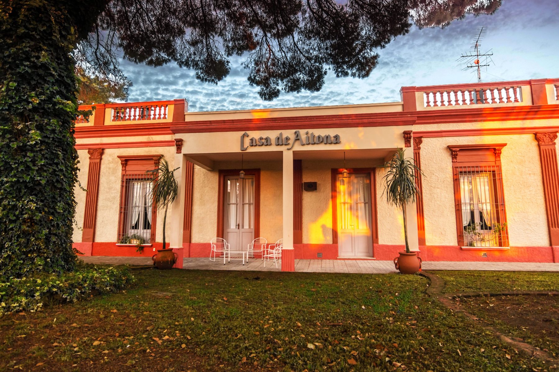 Fachada de la Casa de Aitona al atardecer, con sus puertas altas, sillas de hierro y el parque