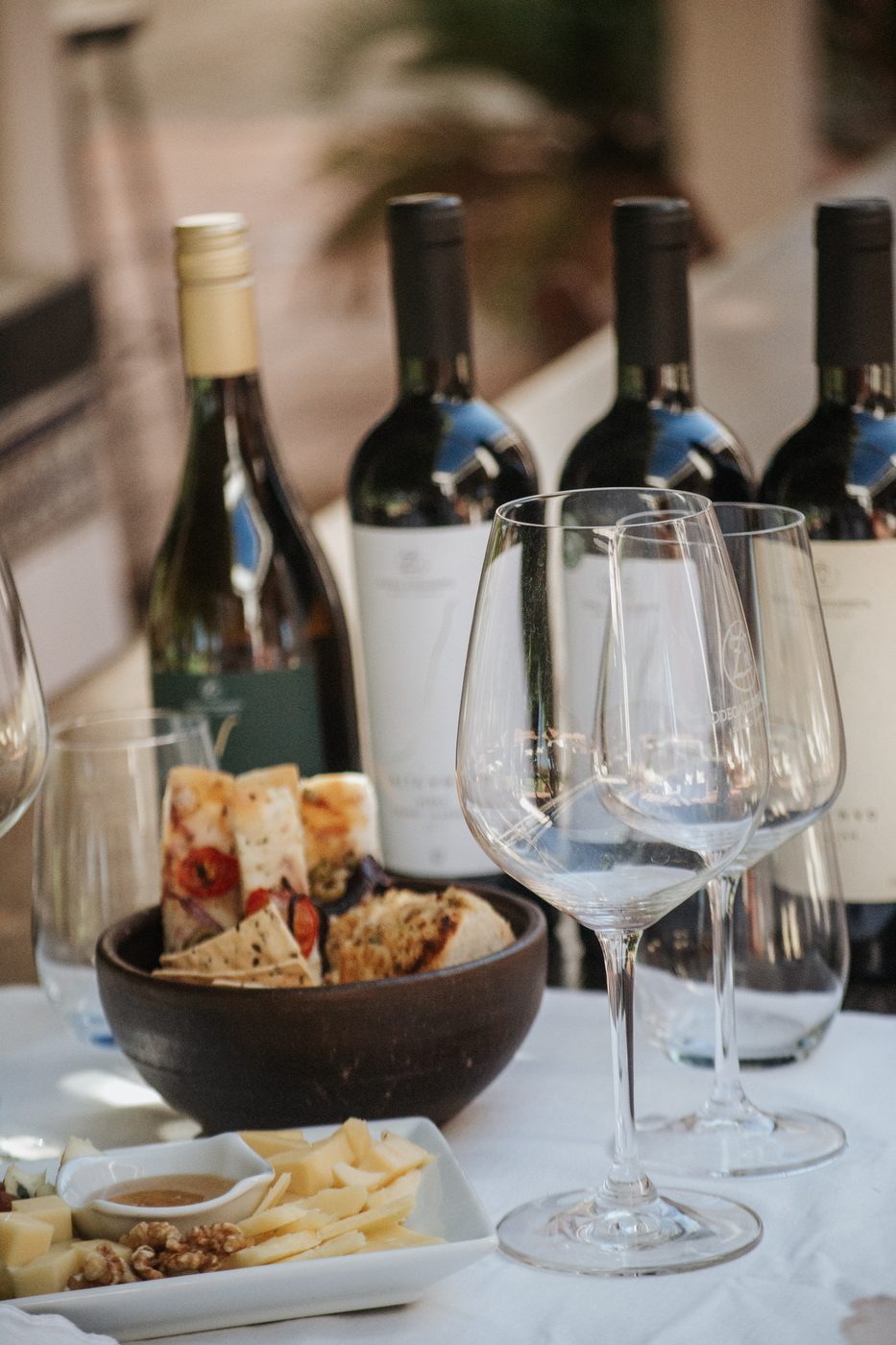 Tabla de quesos y fiambres frente a cuatro botellas y copas en la mesa de degustación